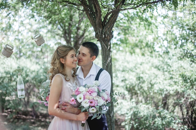 Un joven abraza a su novia sosteniendo un ramo de flores en el verano en la naturaleza