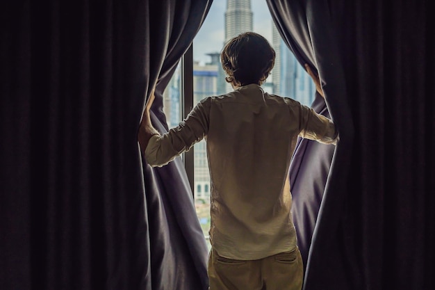 El joven abre las cortinas de la ventana y mira los rascacielos de la gran ciudad.