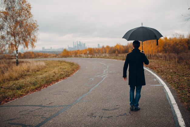 Joven de abrigo negro caminando bajo la lluvia con paraguas