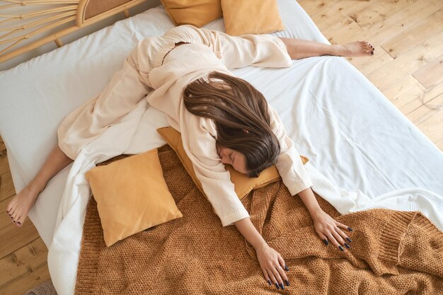 Foto una joven con un acogedor pijama de muselina beige está haciendo yoga en casa en la cama relajada y cerrada