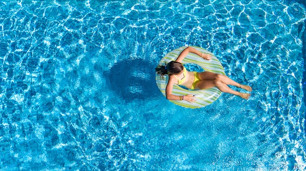 Joven activa en la vista superior aérea de la piscina desde arriba, el niño se relaja y nada en una rosquilla inflable y se divierte en el agua