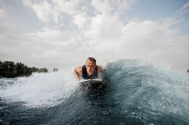 Joven activo tumbado en el wakeboard blanco sobre la ola azul