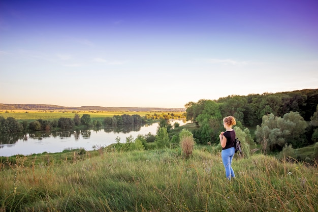 La joven admira la belleza de la naturaleza. Paisaje de verano con río y bosque