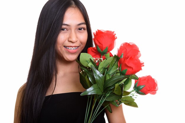 Joven adolescente asiática feliz sonriendo mientras sostiene rosas rojas