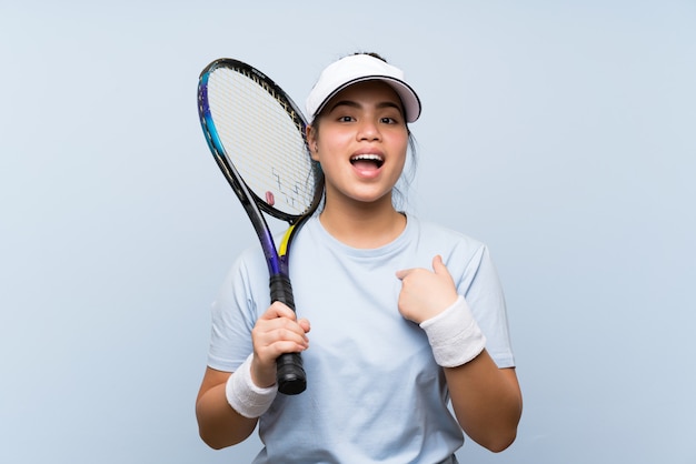 Joven adolescente asiática jugando al tenis con expresión facial sorpresa