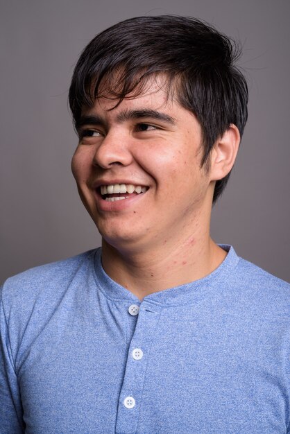 Joven adolescente asiático vistiendo la camiseta azul contra la pared gris