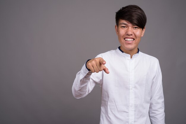 Joven adolescente asiático vistiendo ropa casual elegante contra la pared gris