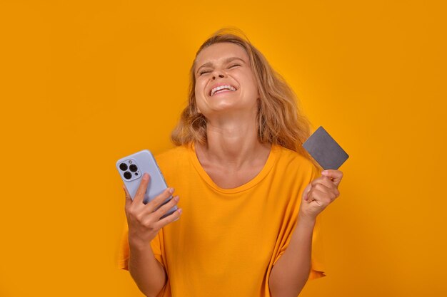 Foto joven adolescente caucásica satisfecha con tarjeta de crédito y teléfono móvil