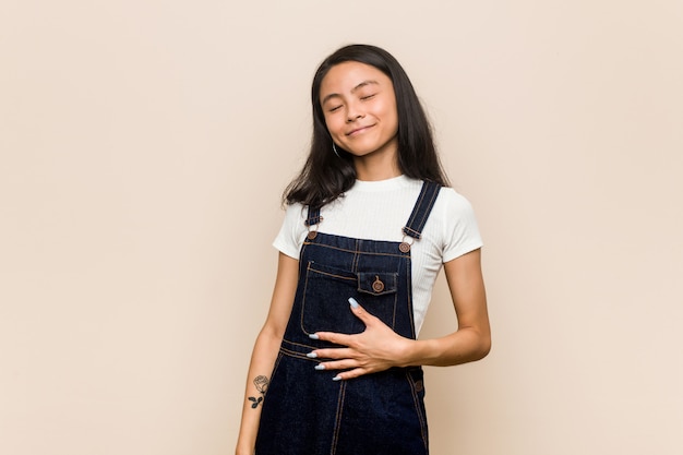 Joven adolescente chino lindo Joven mujer rubia con un abrigo contra un fondo rosa toca el estómago, sonríe suavemente, comer y concepto de satisfacción.