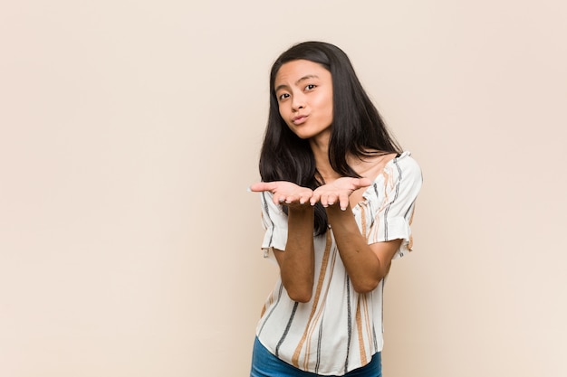 Joven adolescente chino lindo Joven mujer rubia con un abrigo contra una pared de color rosa doblando los labios y sosteniendo las palmas para enviar beso de aire.