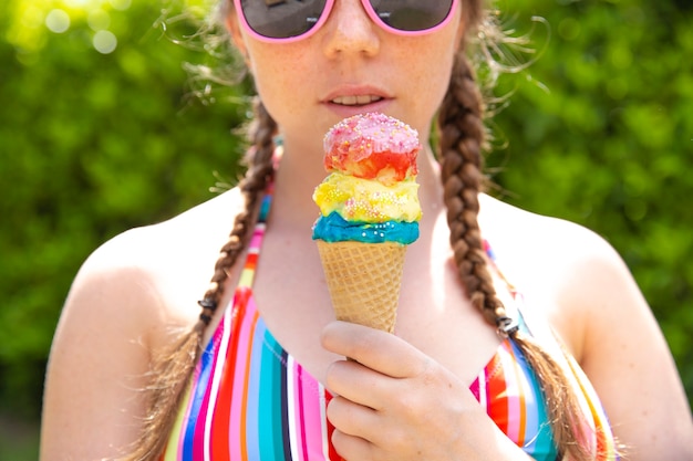 Foto joven adolescente comiendo helado con gafas de sol rosas y trenzas en un caluroso día de verano