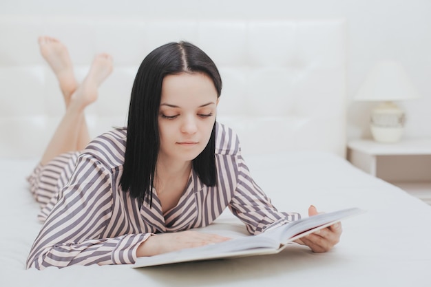 Joven adolescente descalza acostada en su cama leyendo un libro o estudiando