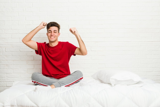 Joven adolescente estudiante hombre cama celebrando un día especial, salta y levanta los brazos con energía.