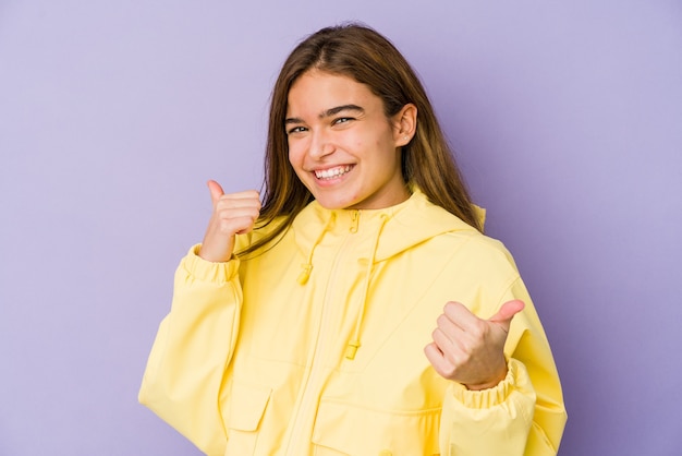 Joven adolescente flaca caucásica en la pared púrpura, levantando ambos pulgares, sonriendo y confiado.