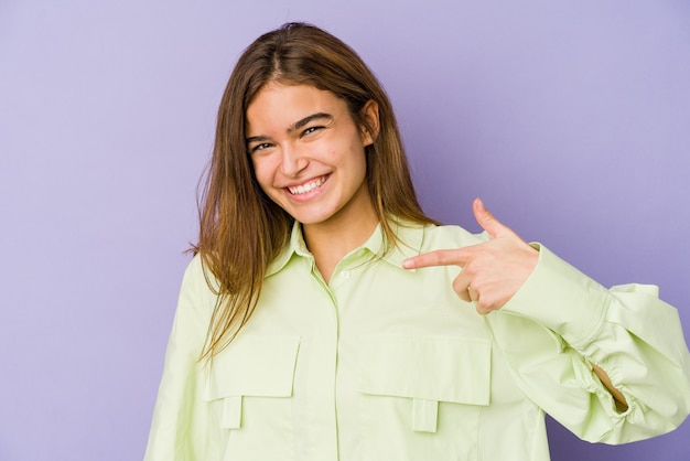 Joven adolescente flaca caucásica en púrpura apuntando con la mano a un espacio de copia de camisa, orgulloso y seguro