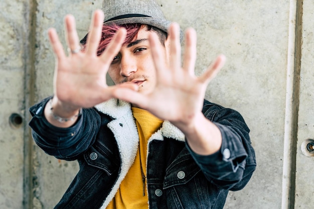 Un joven adolescente haciendo una señal de alto con la palma de las manos y serio detrás de la protesta y el estilo de vida rebelde juvenil casual moderno guapo adolescente retrato de moda en el fondo urbano al aire libre