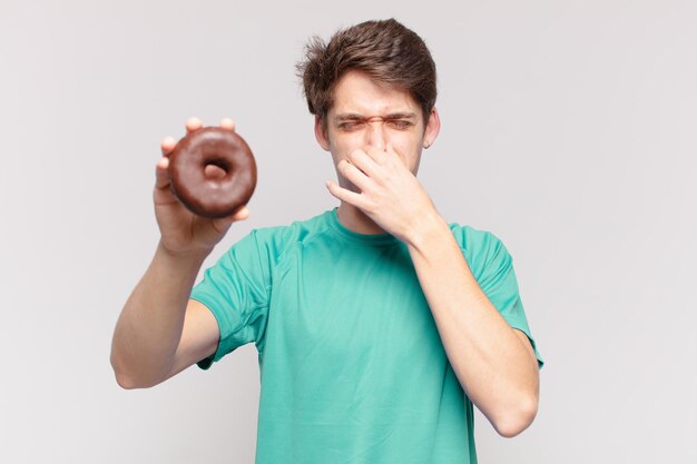 Joven adolescente hombre expresión enojada y sosteniendo un donut