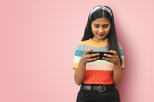 Joven adolescente india asiática sonriendo y jugando juegos en línea en el teléfono móvil o viendo series aisladas con espacio de copia de maqueta