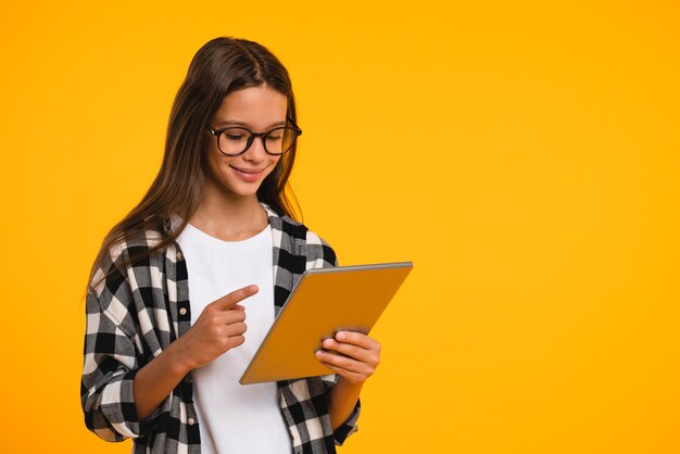 Una joven adolescente inteligente, estudiante, estudiante usando una tableta digital, apuntando a la pantalla, navegando por las páginas web, los medios sociales, los blogs, los vlogs, aislados en fondo amarillo.