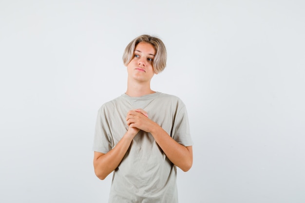 Joven adolescente manteniendo las manos juntas sobre el pecho, mirando hacia arriba en camiseta y luciendo esperanzado. vista frontal.