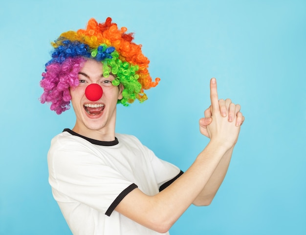 Foto joven adolescente masculino divertido en camiseta blanca sobre fondo azul con peluca de payaso