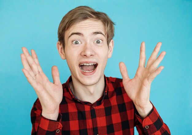 Joven adolescente masculino emocional feliz en camisa roja en la pared azul