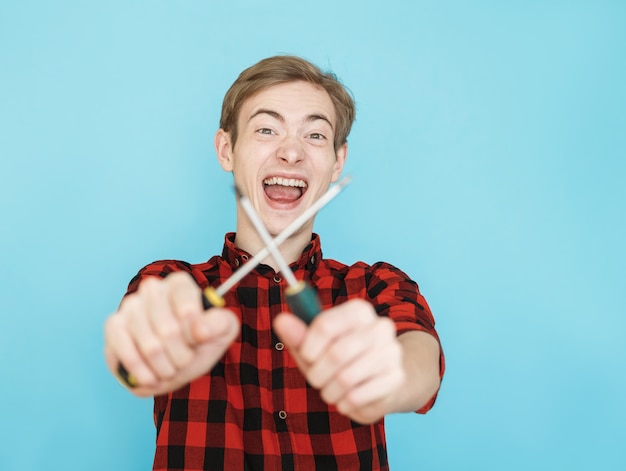 Joven adolescente masculino sonriente en camisa roja en la pared azul pensando con destornillador