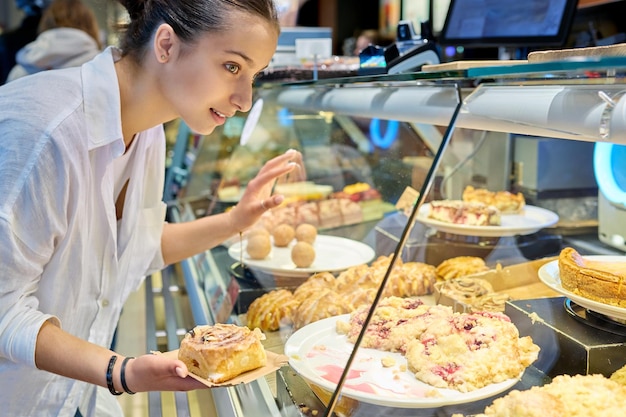 Joven adolescente mirando panes dulces en una vitrina de vidrio en una pastelería