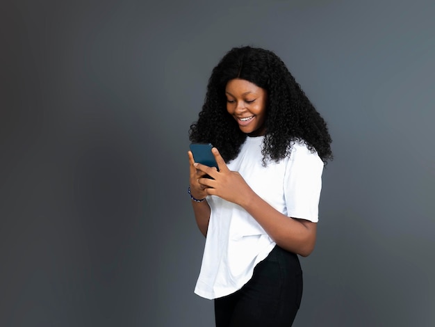 Joven adolescente negra feliz sosteniendo y escribiendo con teléfono móvil