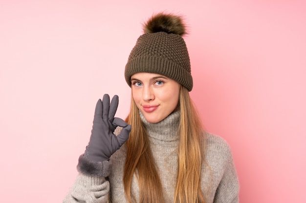 Joven adolescente con sombrero de invierno sobre rosa aislado mostrando un signo bien con los dedos