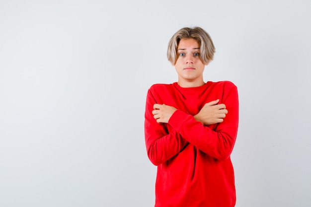 Joven adolescente sosteniendo los brazos cruzados sobre el pecho en un suéter rojo y mirando aterrorizado. vista frontal.