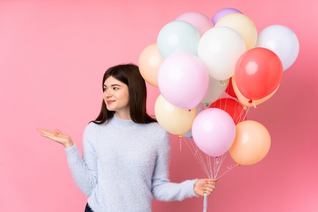 Joven adolescente sosteniendo muchos globos sobre pared rosa con espacio en blanco en la palma