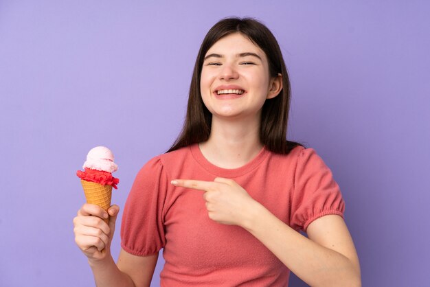 Joven adolescente ucraniana chica sosteniendo un helado de cucurucho sobre pared púrpura y apuntando