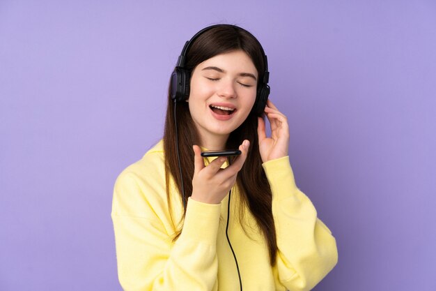 Joven adolescente ucraniana sobre pared púrpura aislada escuchando música con un móvil y cantando