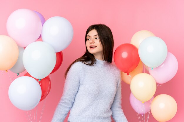 Joven adolescente ucraniana sosteniendo muchos globos sobre pared rosa aislado