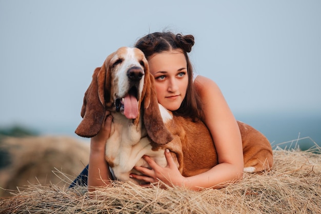 Una joven adulta camina con un perro Basset Hound en la naturaleza. El dueño abraza a la mascota.