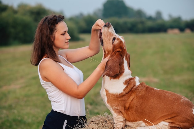 Una joven adulta camina con un perro Basset Hound en la naturaleza El dueño alimenta a la mascota