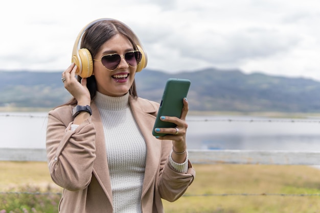 Foto una joven adulta latina con gafas y abrigo está escuchando música cerca del lago