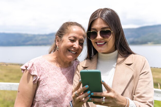 Una joven adulta latina y su madre están mirando el teléfono cerca de un lago