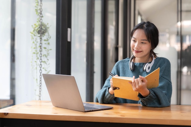 Joven adulto feliz y sonriente estudiante asiático con auriculares hablando en chat en línea reunión usando portátil en el campus universitario o en la oficina virtual estudiante universitaria que aprende a distancia