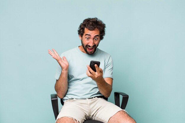 Joven adulto hispano loco usando su teléfono sentado en una silla