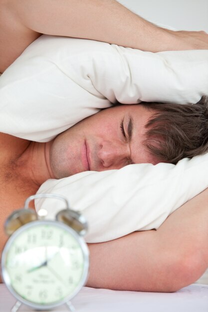 Foto joven adulto masculino estresado por su despertador con la cabeza debajo de la almohada