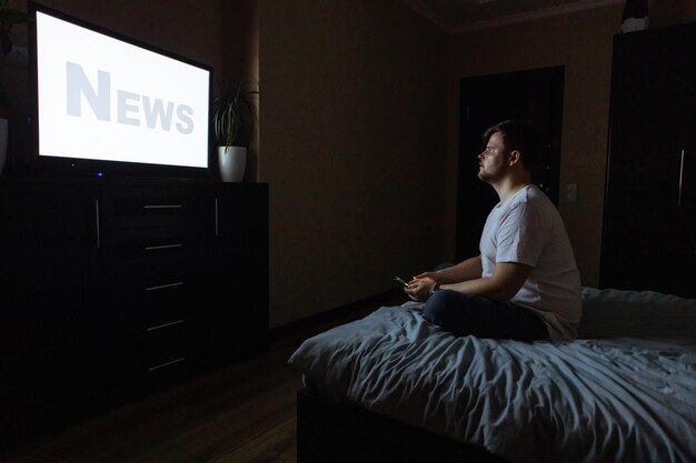joven adulto sentado en la cama mirando la TV