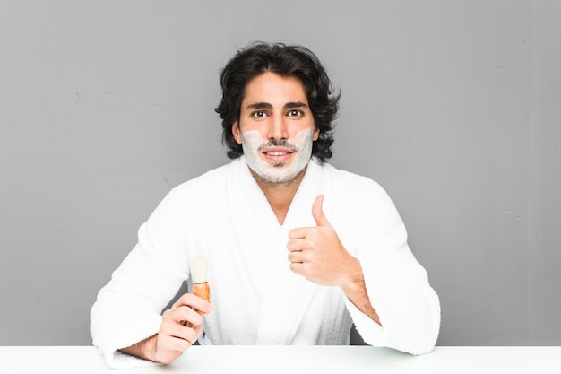 Joven afeitarse la barba sonriendo y levantando el pulgar