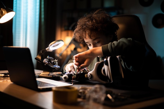 Un joven aficionado al bricolaje construye un robot. El niño se sienta en el escritorio y conecta los cables. El niño está interesado en la robótica.