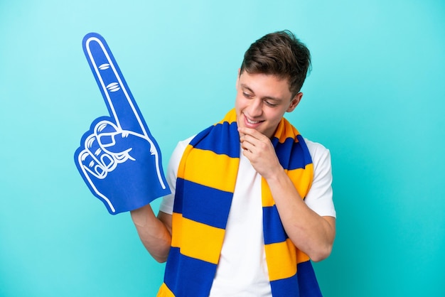 Joven aficionado a los deportes aislado de fondo azul mirando hacia un lado y sonriendo