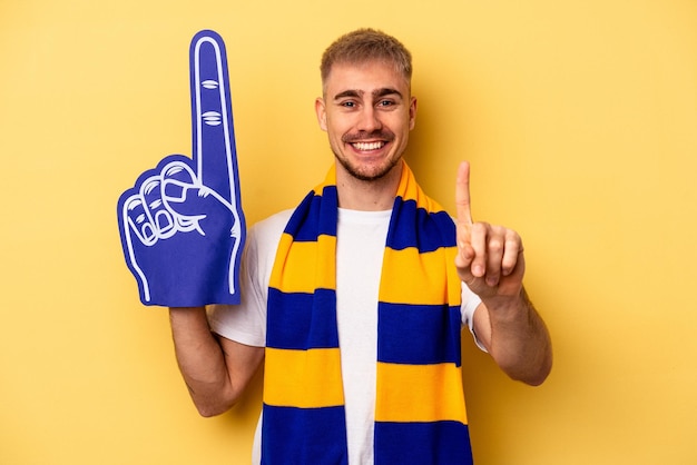 Joven aficionado a los deportes hombre caucásico aislado de fondo amarillo que muestra el número uno con el dedo.