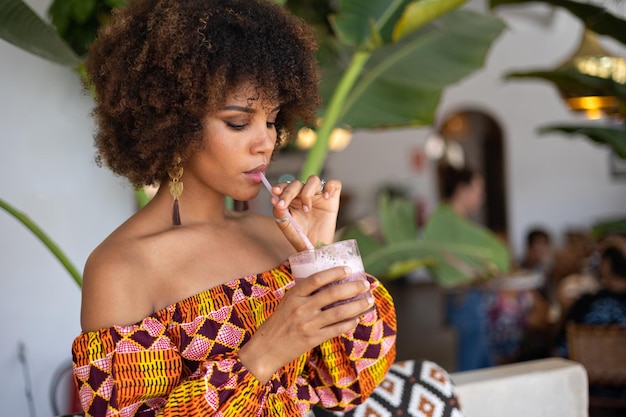 Joven africana bebiendo un batido de frutos rojos en un restaurante tropical