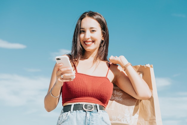 Joven africana con bolsas de compras con teléfonos inteligentes y compras en el centro comercial, concepto de estilo de vida de mujer. Hacer una llamada y enviar mensajes durante el descanso de compras