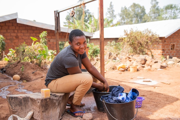 Joven africana lava ropa afuera con jabón y un balde